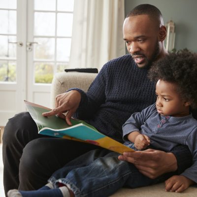 Father And Young Son Reading Book Together At Home